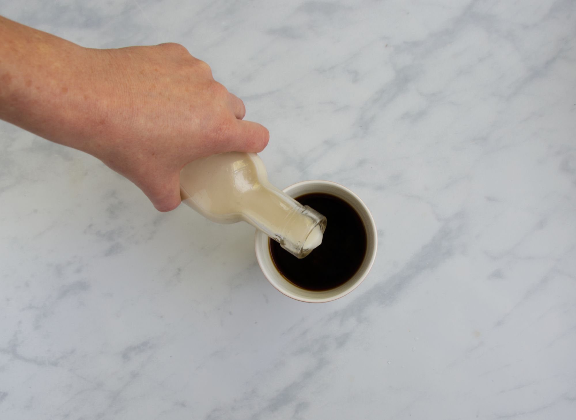 Hand hält Flasche und gieß Milch in den Kaffee